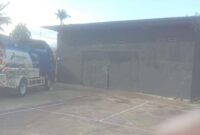 Dokumentasi : Sebuah Bangunan Gudang Dengan Pintu Tertutup. Di Area Sekitar Gudang Juga Tampak Sebuah Mobil Tangki Berlogo Pertamina Terparkir. 