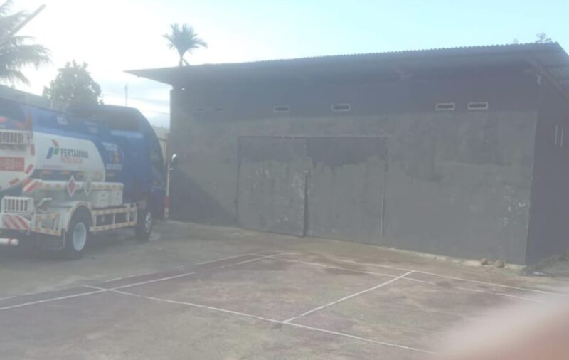 Dokumentasi : Sebuah Bangunan Gudang Dengan Pintu Tertutup. Di Area Sekitar Gudang Juga Tampak Sebuah Mobil Tangki Berlogo Pertamina Terparkir. 
